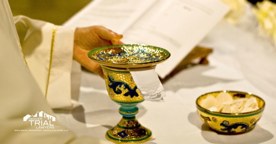 Priest touching a chalice and a bowl of wafers sitting on a table.